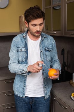 Mutfakta turuncu tutarken antiseptik kullanan yakışıklı bir adam. 