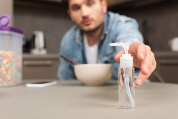 Селективный фокус человека, принимающего дезинфицирующее средство для рук рядом со смартфоном и зерновыми на столе
 