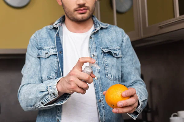 キッチンで手の消毒剤とオレンジを保持している男の作物ビュー — ストック写真