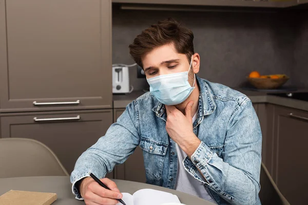 Hombre Máscara Médica Tocando Cuello Mientras Escribe Cuaderno Mesa Cocina —  Fotos de Stock