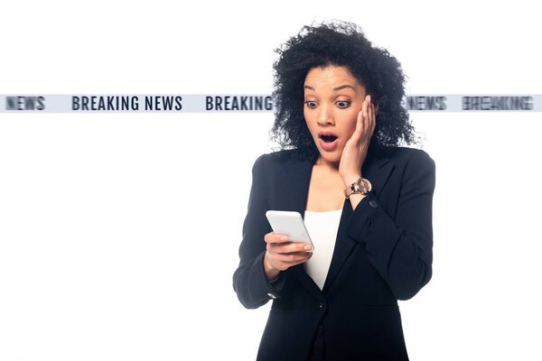 Shocked african american businesswoman with open mouth looking at smartphone isolated on white, breaking news illustration
