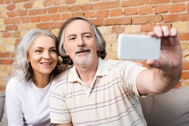Akıllı telefondan selfie çeken mutlu erkek ve kadının seçici odağı 