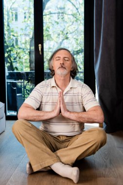 Rahat olgun bir adam, gözleri kapalı ve dua eden eller lotus pozisyonunda oturuyor. 