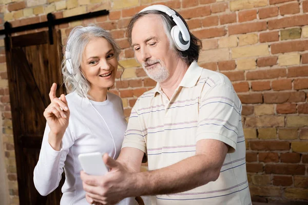 Selective Focus Cheerful Mature Woman Wireless Headphones Pointing Finger Husband — Stock Photo, Image