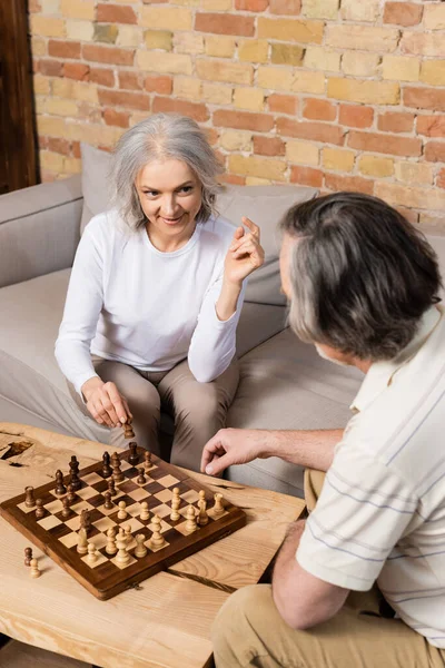 Селективное внимание зрелой женщины и мужчины, играющих в шахматы в гостиной — стоковое изображение Селективное Внимание Зрелой Женщины Мужчины Играющих Шахматы Гостиной — стоковое фото