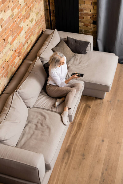 Вид на зрелую женщину, смотрящую кино в гостиной
 