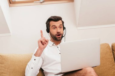 Evde bilgisayardaki görüntülü sohbet sırasında fikri olan heyecanlı kulaklıklı serbest çalışanın seçici odağı.