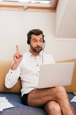 Tişört ve külot giyen heyecanlı bir tele-işçi evde video görüşmesi için kulaklık ve dizüstü bilgisayar kullanırken fikir üretiyor. 