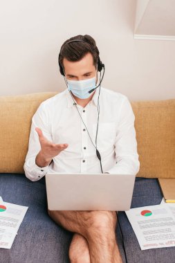 Evde bilgisayardaki video görüşmesi sırasında kulaklık takan tıbbi maske, külot ve tişört giyen serbest çalışan biri. 