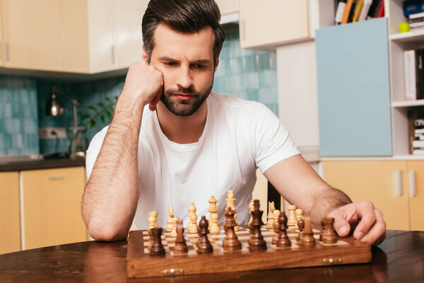 Selective focus of thoughtful man sitting near chess on chessboard on table 