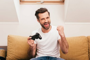 KYIV, UKRAINE - 14 Nisan 2020: Pozitif adam joystick tutuyor ve oturma odasında evet hareketi gösteriyor
