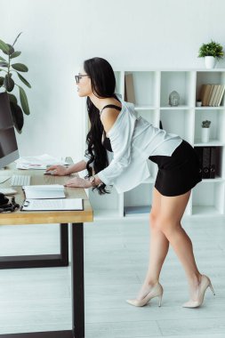 Ofisteki bilgisayarı kullanan seksi sütyenli sekreterin yan görünüşü 