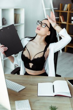 Sütyen giyen seksi sekreterin çalışma masasında pano tutmasının seçici odak noktası 