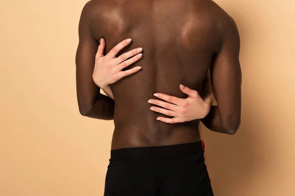 Back cropped view of sexy interracial couple hugging on beige