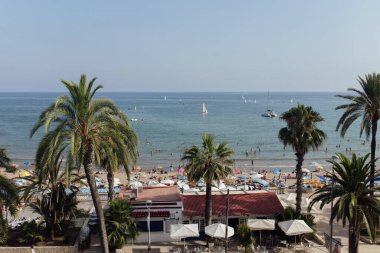 CATALONIA, SPAIN - 30 Nisan 2020: İnsanlar arka planda deniz ve mavi gökyüzü ile plajda dinleniyor