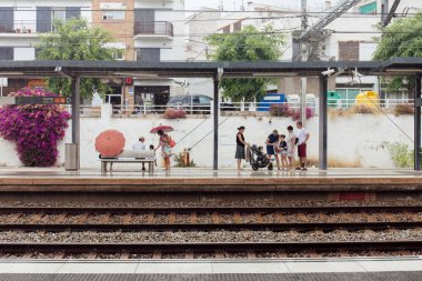 CATALONIA, SPAIN - 30 Nisan 2020: Şemsiyeli insanlar tren istasyonunda bekliyorlar