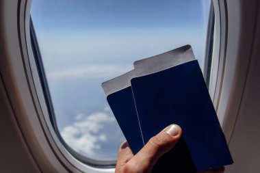 Pasaportları ve uçak lombozunun yanında uçak biletlerini tutan adam görüntüsü.