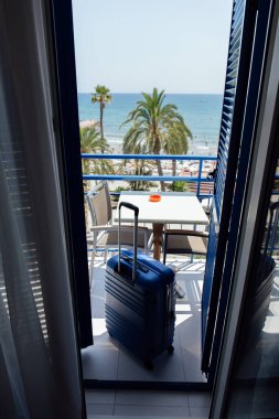 Suitcase on balcony with palm trees and seascape at background in Catalonia, Spain  clipart