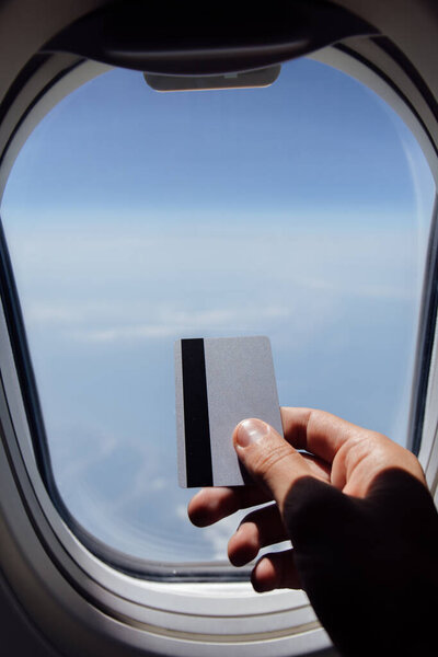 Cropped view of man holding credit card near porthole of airplane 