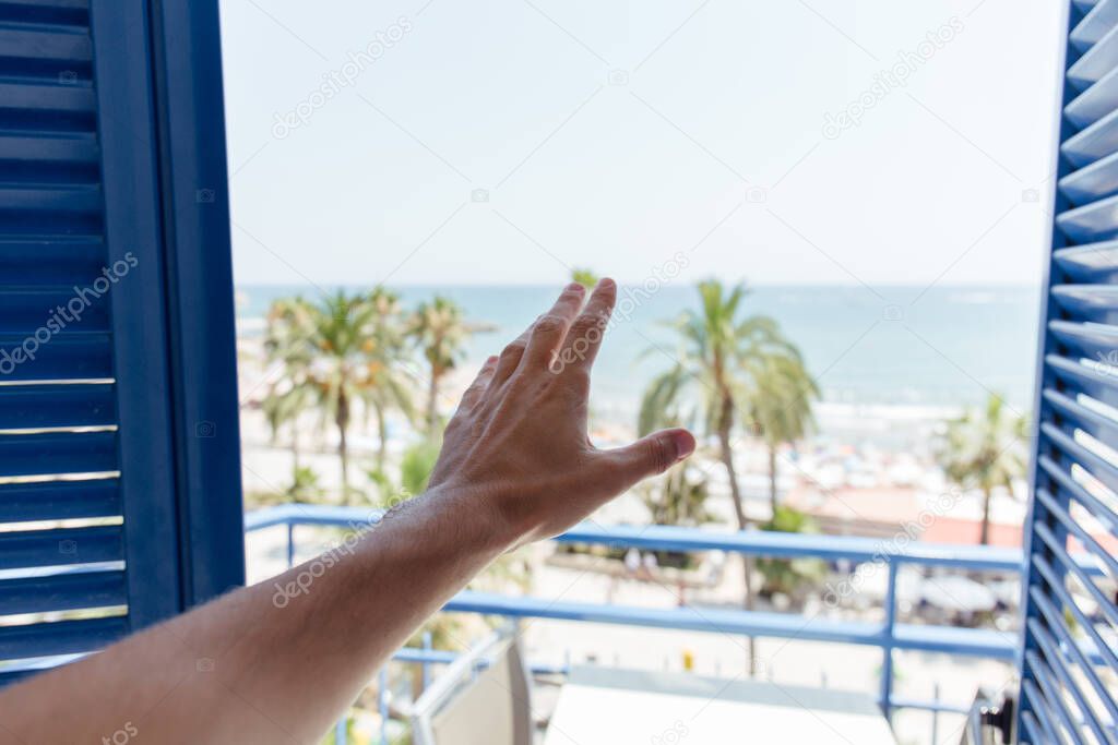 Cropped view of male hand near open door with sea coast and palm trees at background in Catalonia, Spain 