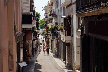 CATALONIA, SPAIN - 30 Nisan 2020: Balkonda bitkileri olan evlerin yakınındaki kentsel caddede yürüyen insanlar