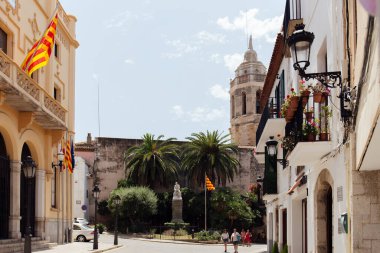 BARCELONA, SPAIN - APRIL 30, 2020: La Senyera flags on buildings on urban street with church of San Bartolome and Santa Tecla and blue sky at background  clipart