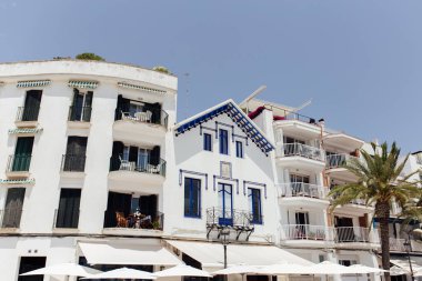 Arka planda açık gökyüzü olan evlerin cephelerinin yanındaki beyaz şemsiyeler, Katalonya, İspanya 
