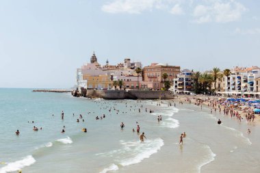 CATALONIA, SPAIN - 30 Nisan 2020: İnsanlar sahildeki binaların ve palmiye ağaçlarının yakınında denizde yüzüyor