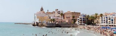 CATALONIA, SPAIN - 30 Nisan 2020: Sahildeki binalar ve palmiye ağaçları yakınında denizde yüzen insanların panoramik mahsulü