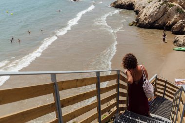 CATALONIA, SPAIN - 30 Nisan 2020: Arka planda kumlu plaj ve deniz ile merdivenlerde duran kadının seçici odak noktası 