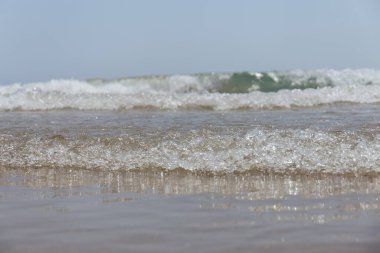 Selective focus of wave on wet sandy beach with blue sky at background clipart