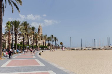 BARCELONA, SPAIN - 30 Nisan 2020: İnsanlar arka planda palmiye ağaçları ve Aziz Bartolomeus Kilisesi ve Santa Tecla Kilisesi yakınlarındaki kaldırımda yürüyorlar