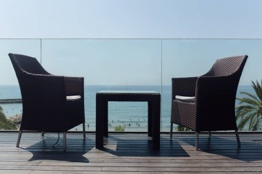 Low angle view of table and chairs near glass fencing and seascape at background in Catalonia, Spain  clipart