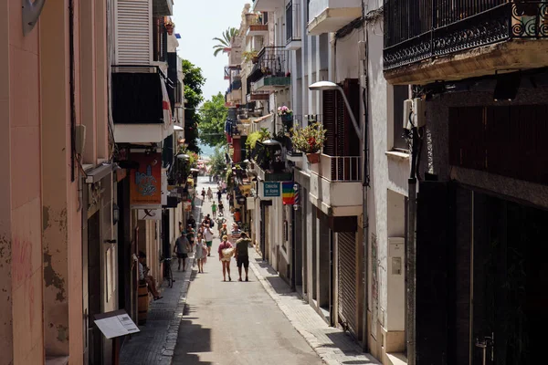 CATALONIA, SPAIN - 30 Nisan 2020: Balkonda bitkileri olan evlerin yakınındaki kentsel caddede yürüyen insanlar
