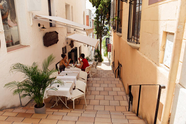 КАТАЛОНИЯ, Испания - 30 апреля 2020 года: Люди, сидящие за столом в кафе под открытым небом возле домов на городской улице
