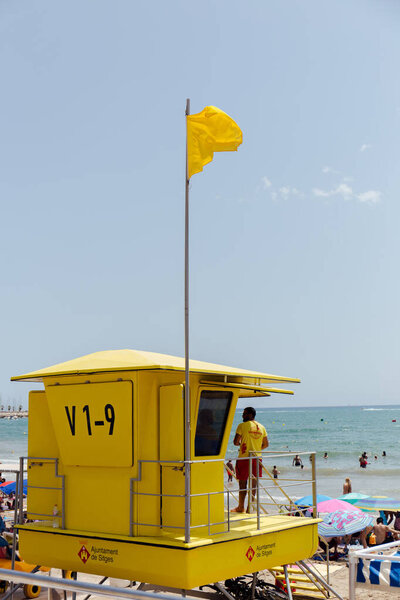 CATALONIA, SPAIN - APRIL 30, 2020: Rescuer standing in lifeguard tower with flag on beach 