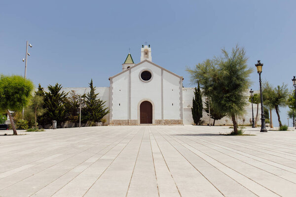 Low angle view of trees near chapel with blue sky at background in Catalonia, Spain