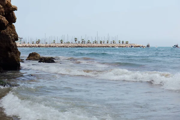 Pietre Onde Marine Sulla Costa Con Molo Barche Sullo Sfondo — Foto Stock