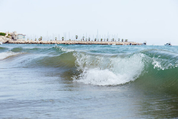 Selective focus of waves on sea coast with pier and palm trees at background, Catalonia, Spain 