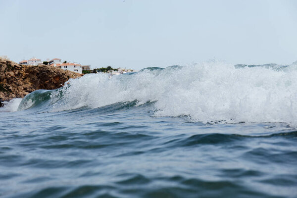 Selective focus of sea wave with houses on coast and blue sky at background in Catalonia, Spain 