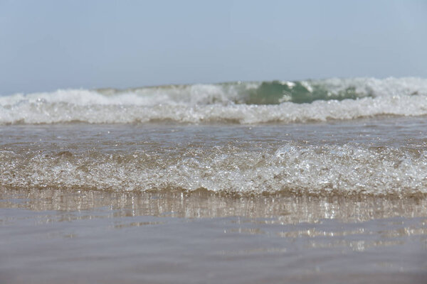 Selective focus of wave on wet sandy beach with blue sky at background