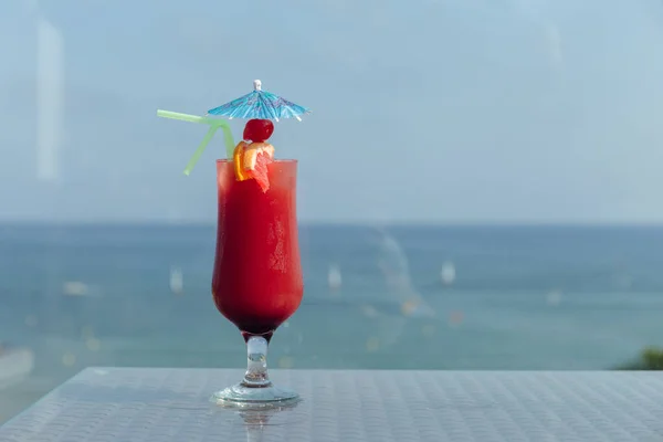 一杯鸡尾酒 配上鸡尾酒伞 喝着餐桌上的稻草 背景是大海和蓝天 — 图库照片