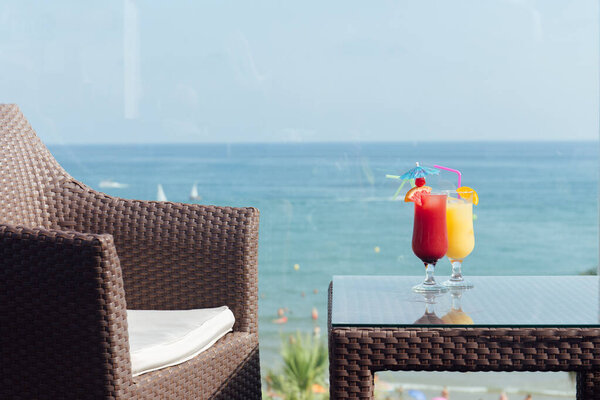 Стаканы коктейлей на столе рядом со стулом с морской накидкой и ясным небом на заднем плане
 