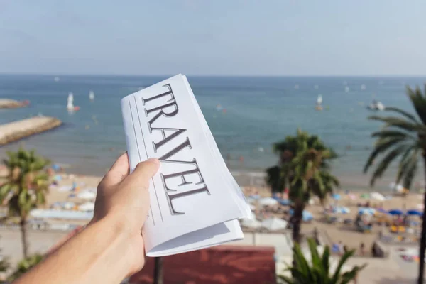 照片上的男人拿着报纸 背景是沙滩上和蓝天上的旅行字母 — 图库照片