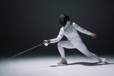 Fencer training under spotlight on black background clipart