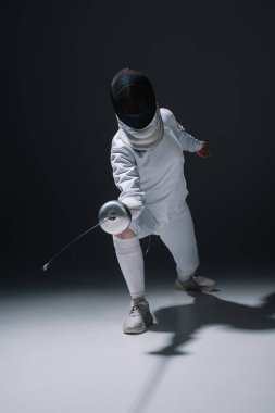 Fencer in fencing mask holding rapier while training on white surface on black background clipart
