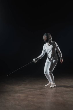 Swordswoman in fencing suit and mask training with rapier on black background clipart
