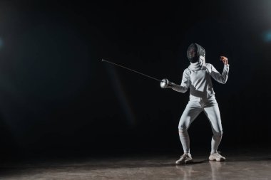 Fencer training with rapier under spotlight on black background clipart
