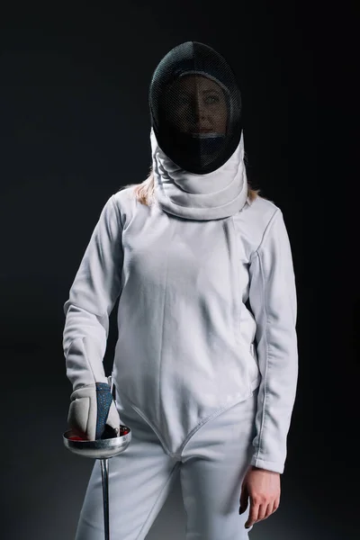 Fencer in fencing mask and suit holding rapier isolated on black