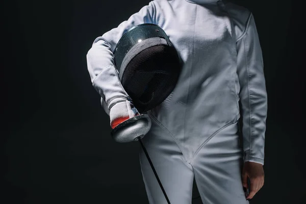 Cropped view of fencer holding fencing mask and rapier isolated on black